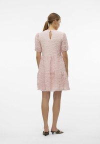 Rosa klänning med puffärmar i texturerat tyg, med detaljer i form av en nyckelhålskärning bak och en volymfylld kjol, matchad med svarta slidesandaler.