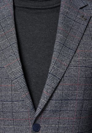 Szary blezer w kratę z ciemnoniebieskimi akcentami i z pojedynczym zapięciem na guzik, nakładany na ciemnoszary golf. Teksturowana tkanina z drobnymi detalami.