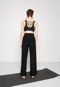 Schwarzes Sportoutfit mit einem Kurz-Top mit überkreuzten Rückenriemen und weit geschnittenen Hosen mit elastischem Bund und seitlicher Reißverschlusstasche.