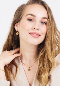 Gouden oorbellen en ketting met cirkelvormige hangers met een letter. Glad texture, minimalistisch ontwerp en delicate ketting.
