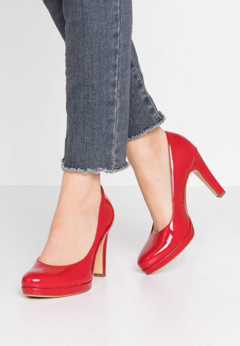 Røde patentlæder højhælede pumps med rund tå, platform og spidse hæle, båret med grå jeans med frynset kant.