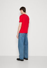 T-shirt rouge à manches courtes associé à un jean léger et ample bleu clair. La tenue est complétée par des chaussures noires. Design simple sans motifs.