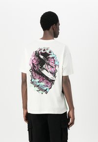 White cotton T-shirt featuring a vibrant graphic of a surfer with bold colors, abstract shapes, and a patterned background. Short sleeves.