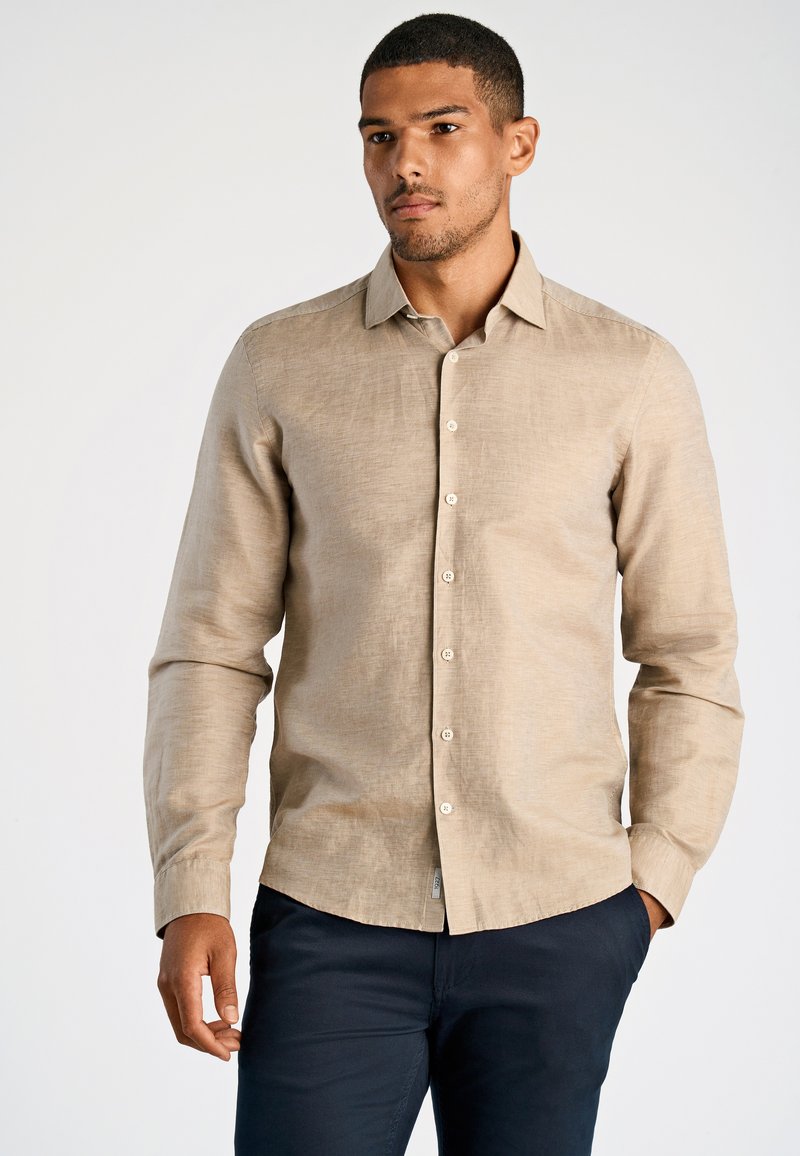 Lichtbeige shirt met lange mouwen van gestructureerde stof, met een knoopsluiting aan de voorkant en een afgeronde zoom, gecombineerd met donkerblauwe broek.