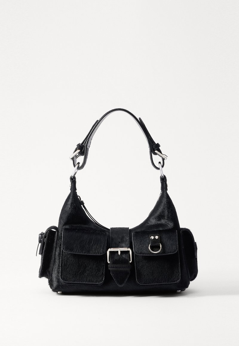 Bolso de mano negro hecho de cuero texturizado con una correa curvada, dos bolsillos frontales, herrajes plateados y un detalle de hebilla central.