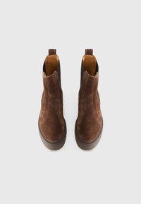Botas de tobillo de ante marrón con paneles laterales elásticos, puntera redonda y suela de goma gruesa. Presenta costuras mínimas y una pestaña en la parte posterior.
