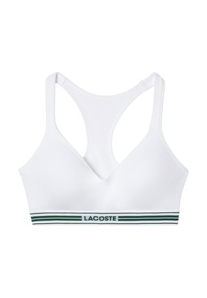 Top sportivo bianco con scollatura a V, caratterizzato da un bordo striato verde nella parte inferiore con il testo "LACOSTE". Tessuto liscio e stile a corsetto.