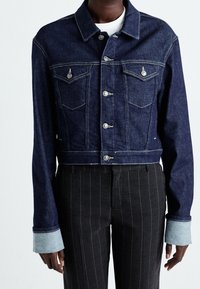 Mörk denim jacka med kort modell och silverfärgade knappar, två bröstfickor och kontrasterande ljusblå detaljer vid ärmsluten. Matchas med randiga byxor.