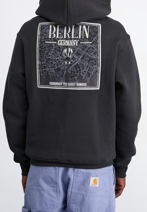 Černá mikina s kapucí s grafikou mapy Berlína, teplovzdušným balónem, siluetami lidí a nápisy „Berlin Germany“ a „Remember the Candy Bomber“ na zádech.