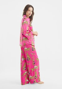 Růžový pyžamový set s leopardím potiskem, obsahující detaily jako desky a nápoje. Vyrobeno z hladké tkaniny, s volnými kalhotami a tričkem.