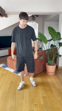 Outfit casual composto da una maglietta nera a maniche corte con taschino e pantaloni shorts in denim neri, abbinati a scarpe sportive argentate e calze bianche.
