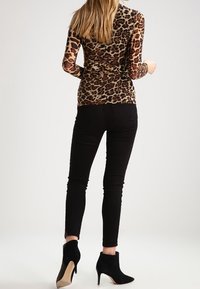 Pitkähihaisessa, läpinäkyvässä seeprakuosisessa paidassa, mustat slim-fit farkut ja mustat nilkkurit, joissa on taupe-väriinen korko.