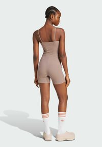 Bodysuit marrón con canalé, tirantes finos, diseño ajustado y piernas cortas. Combinado con calcetines blancos con rayas naranjas y calzado beige.