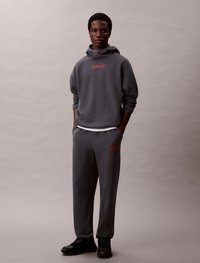 Set di felpa grigia e pantaloni sportivi in cotone, con il logo rosso "Calvin Klein". Sneakers nere completano l'outfit.