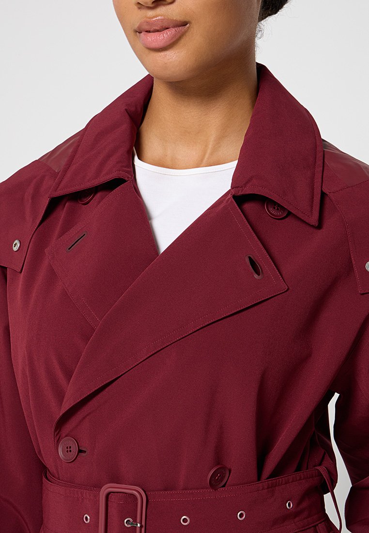 Bordeaux trenchcoat met een dubbel-breasted ontwerp, grote kraag en knopen; heeft een ceintuur in de taille en glanzende accenten op de schouders.