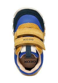 Zapatilla multicolor con paneles azules, amarillos y marinos. Presenta dos correas de Velcro y una suela texturizada. Marca visible en el lado.