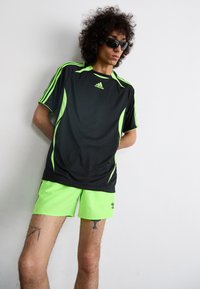 Sort atletisk T-shirt med neongrønne detaljer, med korteærmer og logo. Sammen med matchende neongrønne shorts og solbriller.