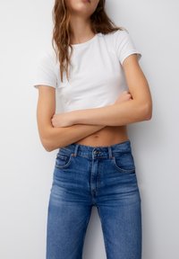 T-shirt blanc à manches courtes associé à un jean en denim bleu taille haute. Le jean présente des poches classiques et une fermeture à boutons.