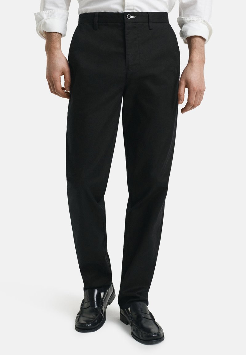 Pantaloni neri in cotone con taglio dritto, dotati di zip e chiusura con bottone, e tasche frontali. Texture liscia e colore uniforme.