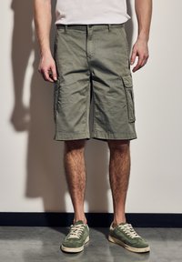 Olivově zelené cargo šortky s několika bočními kapsami, volným střihem a směsovým bavlněným materiálem. Jsou vybaveny prošívanými detaily a knoflíkem na pase.