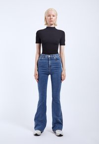 Black fitted short-sleeve top paired with high-waisted blue flared jeans, featuring a classic denim texture and subtle stitching details.