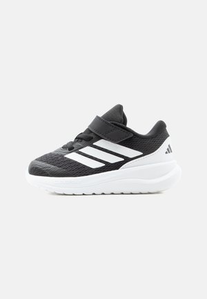 Czarno-białe sportowe buty typu sneaker z siateczkową cholewką, paskiem na rzep, detalami z sznurowadłami i grubą białą wyściełaną podeszwą.
