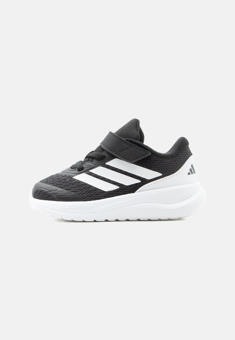 Baskets de sport noir et blanc avec dessus en mesh, bride velcro, détails de lacets et semelle blanche épaisse et rembourrée.