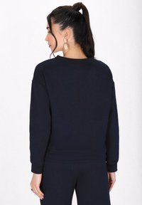 Felpa blu navy a trama con motivo geometrico, polsini a coste e vestibilità rilassata. Vista da dietro con acconciatura a coda di cavallo laterale.