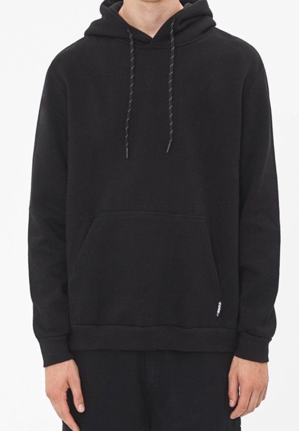 Homme portant un sweat à capuche noir uni avec des cordons et une poche kangourou frontale, debout devant un fond blanc.