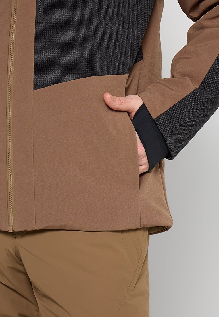 Veste marron et noire avec un panneau supérieur texturé, fermeture éclair et poche latérale ; tissu lisse et coupe ajustée.