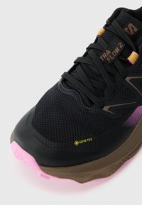 Černá sportovní bota s texturovaným síťovaným svrškem, značkou GORE-TEX, růžovou gumovou podrážkou a fialovými akcenty. Obsahuje vyztuženou špičku.