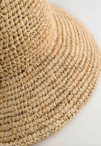 Lichte beige strohoed met een brede rand en een geweven ontwerp, voorzien van getextureerde, cirkelvormige patronen en een zachte afwerking.
