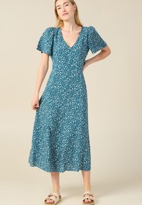 Teal Kleid mit Blumenmuster, kurzen Puffärmeln, V-Ausschnitt und fließender A-Linie. Leichter Stoff mit kleinen weißen und blauen Blumen.