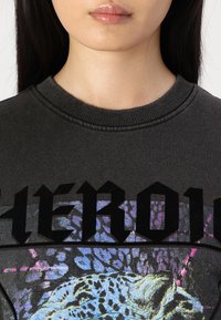 Felpa nera con scollatura rotonda e stampa grafica intricata con design di leopardo, accentuata da dettagli blu e viola.