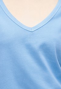 Ανοιχτό μπλε μπλουζάκι με λαιμόκοψη σε σχήμα V, φορεμένο σε ανοιχτόχρωμο δέρμα, που δείχνει το πάνω μέρος του στήθους και την περιοχή του λαιμού.