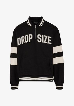 Pull-over noir à zip avec le texte "DROP SIZE", rayures blanches sur les manches et l'ourlet, tissu doux et poche avant. Détail de col rayé.
