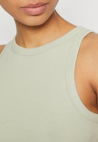 Světle zelen ý žebrovaný top bez rukávů s vysokým výstřihem, který se pyšní přiléhavým střihem a jemnou texturou. Bez viditelných kovových prvků či zdobení.