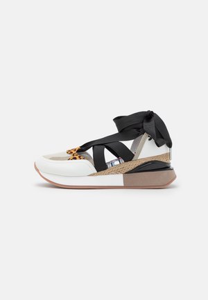 Biały sneaker z czarnymi krzyżującymi się paskami, motywem w panterkę, plecioną środkową podeszwą oraz grubą gumową podeszwą z beżowymi i czarnymi akcentami.