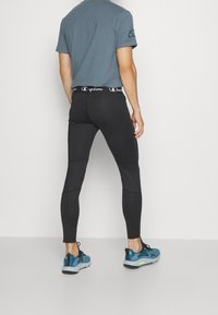 Szary T-shirt i czarne legginsy sportowe z logo Champion na pasku. Osoba nosi niebieskie buty sportowe z czarnymi akcentami.