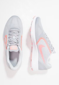 Sneaker sportive grigie con accenti rosa, caratterizzate da una tomaia in rete, design con lacci e una suola bianca texturizzata con punti di trazione rosa.