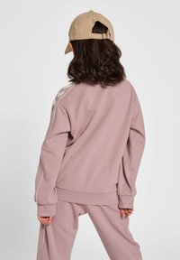 Mjukt rosa sweatshirt med vita sidostripes, lös passform och ribbade ärmslut, i kombination med matchande byxor. Beigekeps med spänne.