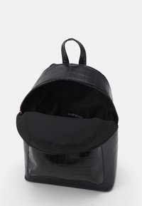 Czarny plecak z sztucznej skóry o fakturze krokodylej, z zamkiem błyskawicznym, uchwytem na górze oraz czarnym wnętrzem z materiału. Posiada jedną komorę.