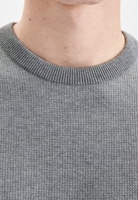 Pull gris côtelé avec un col rond, présentant une texture douce et un motif uniforme sur toute la surface. Léger, coupe décontractée.