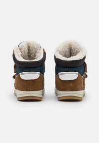 Bruna mockason och blå tyg högtoppsskor med vita detaljer, som har en mjuk fleecefoder och en texturerad gummisula.