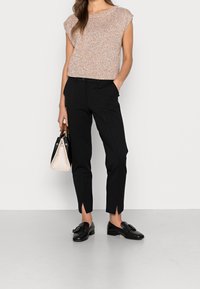 Pull à manches courtes légèrement texturé, mélange de rose et beige, associé à un pantalon noir slim avec fentes latérales et des mocassins noirs.