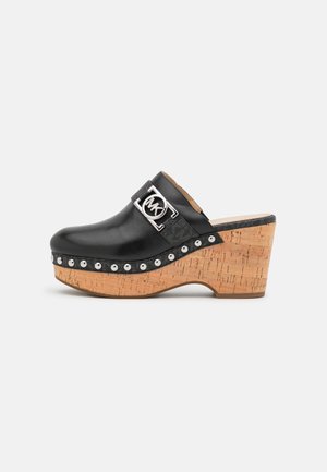 Sabot en cuir noir avec une plateforme en liège, ornée d'un logo métallisé et de clous argentés le long du bord. Texture lisse et bout arrondi.