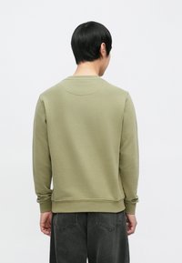 Olivengrønn genser med rund hals, lange ermer og ribbestrikkede mansjetter. Synlig tekstur, minimalistisk design uten mønstre eller detaljer.