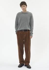 Pulover gri tricotat și pantaloni din catifea cord cu un brâu negru. Încălțăminte închisă la culoare. Design simplu, croială relaxată și texturi ribbate.