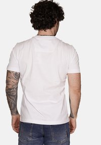 Maglietta bianca in cotone con maniche corte, design aderente e colletto rotondo. La vista posteriore mostra una texture liscia e nessun motivo.