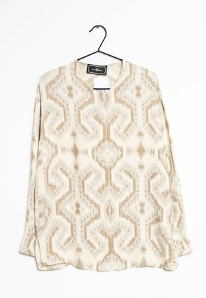 Blouse à manches longues en tissu léger, présentant un motif géométrique répétitif beige et crème, avec un col rond et des fentes sur les côtés.